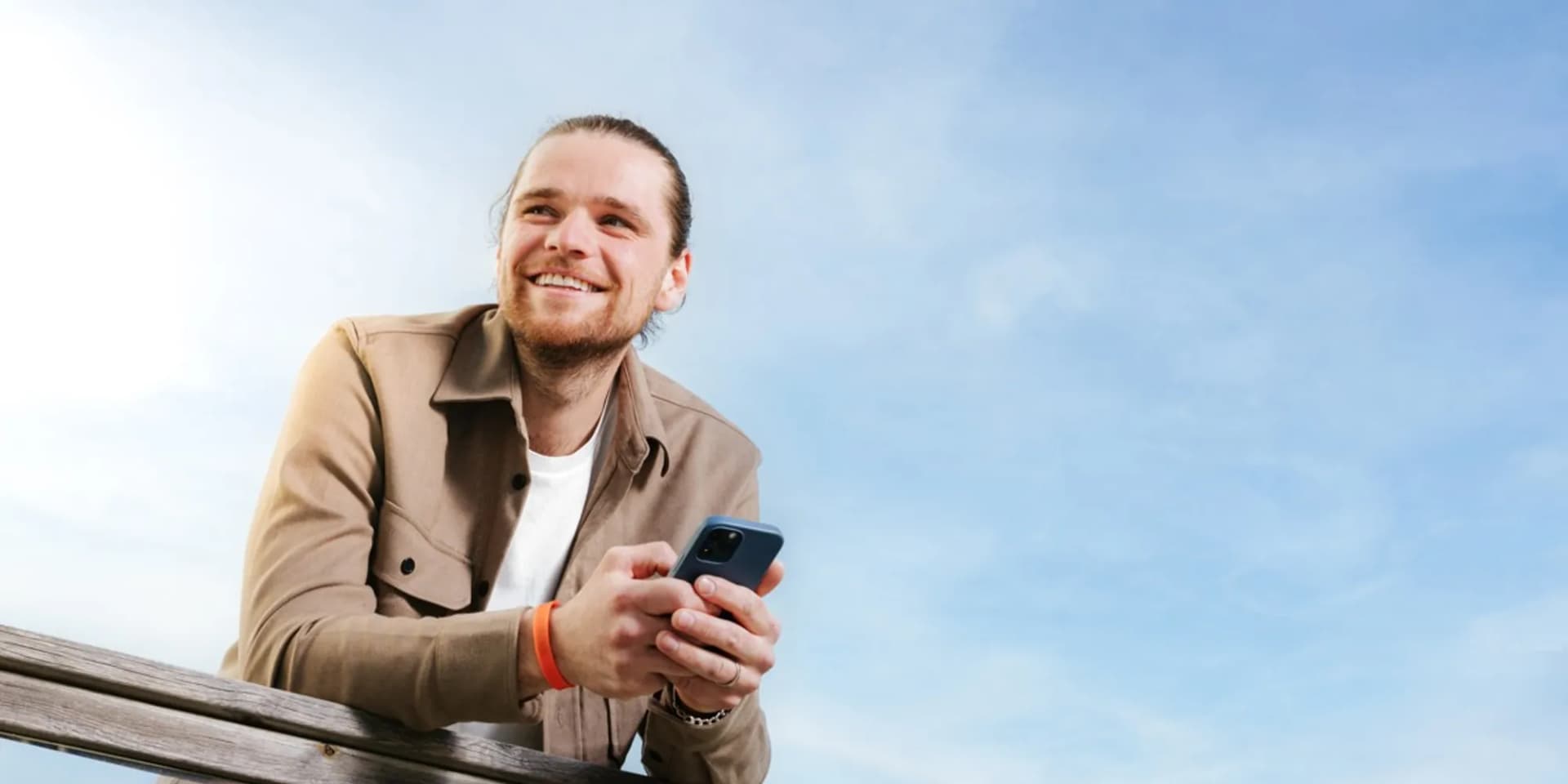 En man sitter på en bänk och tittar på sin mobiltelefon.