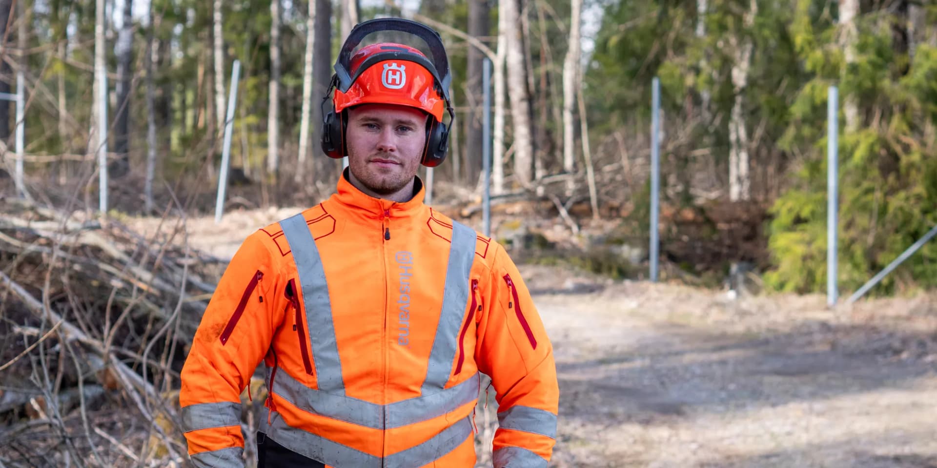 En man i en orange overall som står i skogen.