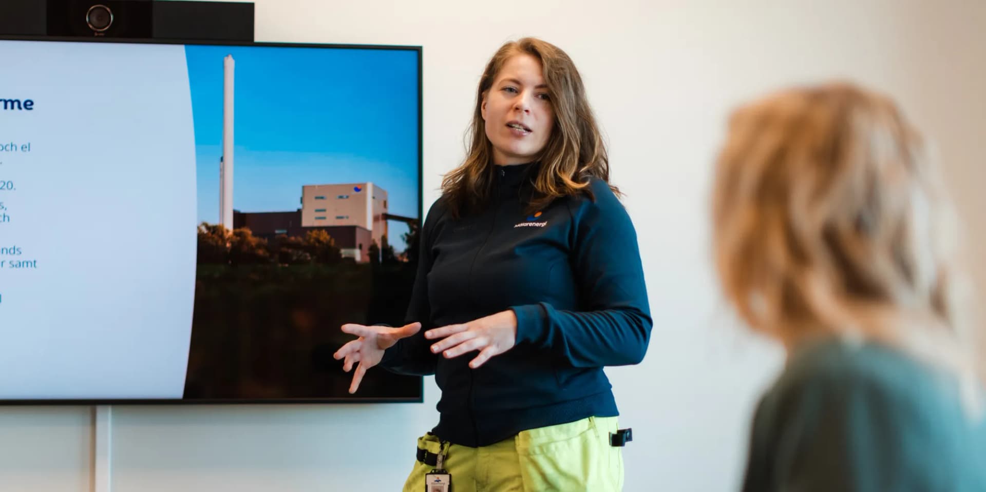 En kvinna i varselbyxor står och håller i en presentation